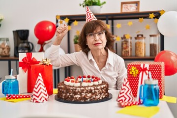 Wall Mural - Middle age woman celebrating birthday holding big chocolate cake annoyed and frustrated shouting with anger, yelling crazy with anger and hand raised