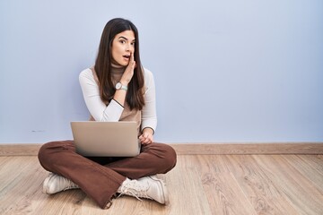 Sticker - Young brunette woman working using computer laptop sitting on the floor hand on mouth telling secret rumor, whispering malicious talk conversation