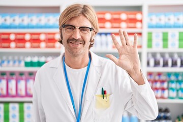 Wall Mural - Caucasian man with mustache working at pharmacy drugstore showing and pointing up with fingers number five while smiling confident and happy.