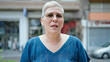 Middle age grey-haired woman standing with serious expression at street
