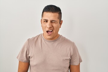 Poster - Hispanic young man standing over white background winking looking at the camera with sexy expression, cheerful and happy face.