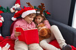 © Krakenimages.com - Brother and sister reading book sitting on sofa by christmas decoration at home