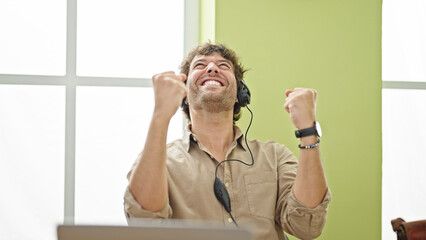 Canvas Print - Young hispanic man business worker using laptop and headphones celebrating at office