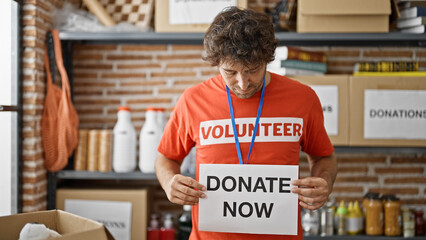 Canvas Print - Young hispanic man volunteer holding donate now banner at charity center