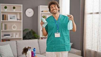 Wall Mural - Young hispanic man professional cleaner holding cloth and sprayer smiling at home