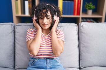 Sticker - Young middle eastern woman listening to music sitting on sofa at home