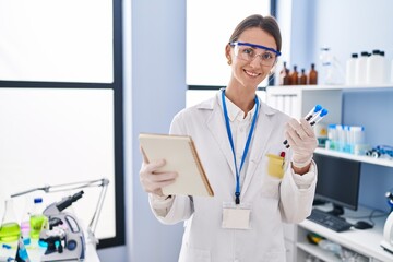 Canvas Print - Young caucasian woman scientist holding test tubes reading notebook at laboratory