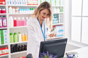 Poster - Young beautiful hispanic woman pharmacist using computer holding pills bottle at pharmacy