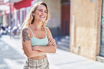 Wall Mural - Young blonde woman standing with arms crossed gesture at street