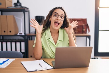 Sticker - Young hispanic woman working at the office wearing glasses celebrating crazy and amazed for success with arms raised and open eyes screaming excited. winner concept