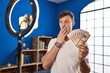 © Krakenimages.com - Caucasian man recording vlog tutorial with smartphone at home holding money covering mouth with hand, shocked and afraid for mistake. surprised expression