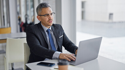 Poster - Young hispanic man business worker wearing glasses using laptop at office