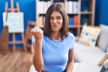 Wall Mural - Brunette young woman sitting on the sofa at home angry and mad raising fist frustrated and furious while shouting with anger. rage and aggressive concept.