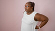 Worried african american woman, plus size with braids, standing alone, suffering serious backache over isolated pink background. worry of spinal injury showing on her hurting face.