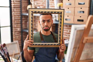 Poster - Young hispanic man sitting at art studio with empty frame depressed and worry for distress, crying angry and afraid. sad expression.