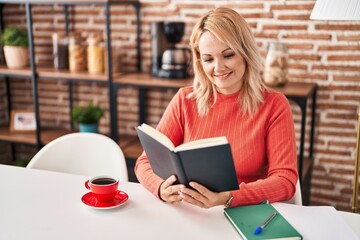 Canvas Print - Young blonde woman reading book and drinking coffee at home