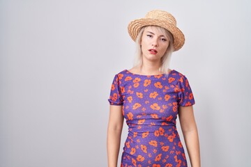 Poster - Young caucasian woman wearing flowers dress and summer hat looking sleepy and tired, exhausted for fatigue and hangover, lazy eyes in the morning.