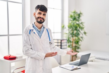 Poster - Young hispanic man wearing doctor uniform doing welcome gesture with hands at clinic