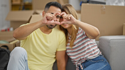 Sticker - Man and woman couple sitting on floor doing heart gesture at new home