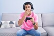 © Krakenimages.com - Hispanic young man playing video game holding controller sitting on the sofa shocked covering mouth with hands for mistake. secret concept.