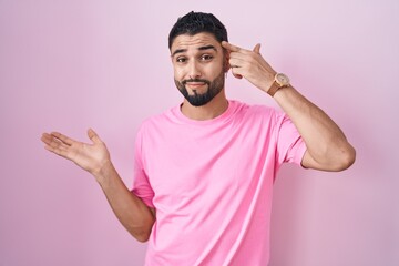 Canvas Print - Hispanic young man standing over pink background confused and annoyed with open palm showing copy space and pointing finger to forehead. think about it.