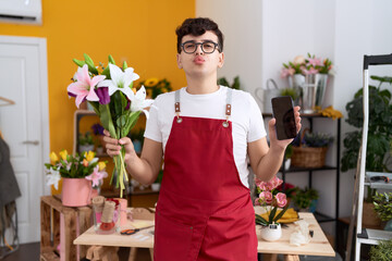 Poster - Young non binary man working at florist shop showing smartphone screen looking at the camera blowing a kiss being lovely and sexy. love expression.