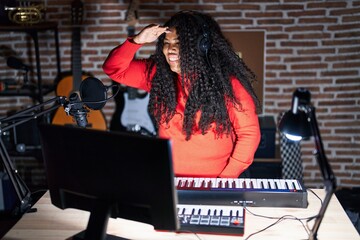 Poster - Plus size hispanic woman playing piano at music studio very happy and smiling looking far away with hand over head. searching concept.