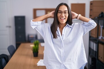 Canvas Print - Young hispanic woman at the office relaxing and stretching, arms and hands behind head and neck smiling happy