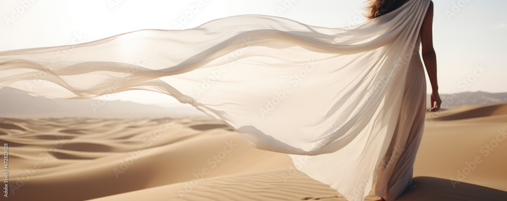 Woman in a long white dress walking in the desert with flowing fabric ...