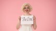 © kinomaster - Portrait of a woman holding a poster with the inscription of the end. Woman in the look of in studio on pink background close up.