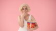 © kinomaster - Portrait of an emotional woman crying with a big bucket of popcorn close up. Woman in the image of crying while watching a dramatic movie in studio on pink background.