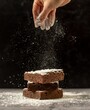 Hand sprinkled sugar onto three stacked brownies covered in powdered sugar