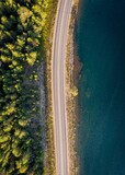 Fototapeta Na ścianę - Aerial view of a road near a lush forest and the tranquil body of water.