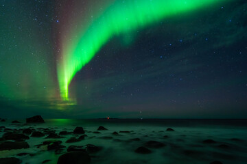 awesome northern lights over the beach, reflection in the silky water. lofoten islands, norway.