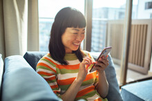 Young Japanese woman using smartphone on sofa