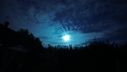 Wall Mural - Timelapse footage of the full moon rising in blue dusk sky among the heavy clouds