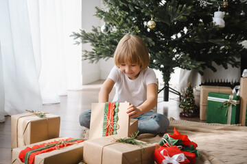 Little boy celebrating Christmas at home unpacking gifts. Christmas lifestyle theme.