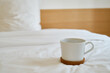 © Iuliia Pilipeichenko - White cup with coffee or tea on the bed. Cozy morning photo. The concept is cozy and warm. Place for text