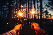 two hands holding sparklers against the background of a night forest reflecting the onset of Christmas