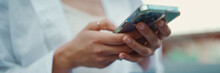Closeup Of Young Woman Holds Smartphone In Her Hands And Scrolls Through The News Feed. Close-up Of Girl Hand Uses Mobile Phone Outdoors
