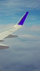 Canvas Print - Wing of an airplane flying in the blue cloudy sky, vertical shot