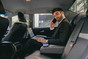 Wall Mural - Busy entrepreneur working on laptop and talking on phone while going to airport by car