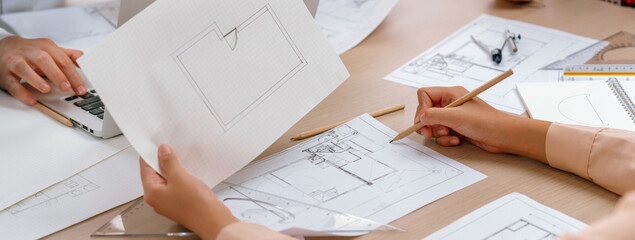 Skilled architect drafts blueprint on paper while male engineer works on laptop in architectural office. Professional engineer and architect collaborate on architectural project. Closeup. Delineation.