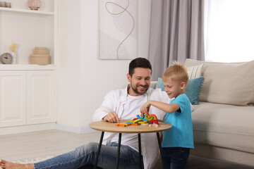 Sticker - Motor skills development. Happy father helping his son to play with colorful wooden arcs at coffee table in room. Space for text