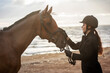 Equestrian sports. Horsewoman and her horse on the beach, portrait on the background of the sea, horseback riding outdoors