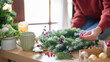 Young asian woman in sweater making christmas wreath and decorations with fir pine branch and red berries while prepare ornaments to celebrate for christmas festive holiday and winter seasons at home