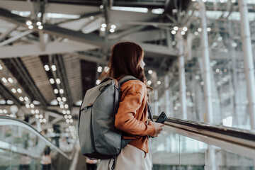 Wall Mural - Young asian woman in international airport terminal or modern train station. Backpacker passenger female commuter walking on escalator