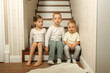 © Ala - two brothers and sister sitting on the stairs in a cozy wooden house