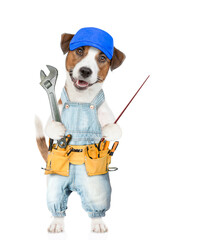 Poster - Funny Jack russell terrier puppy wearing blue cap and denim overalls with tool belt holds adjustable wrench points away on empty space. isolated on white background