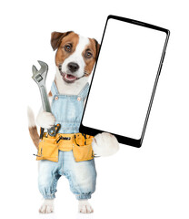 Poster - Funny puppy wearing denim overalls with tool belt holding adjustable wrench and showing big smartphone with white blank screen in it paw. Isolated on white background
